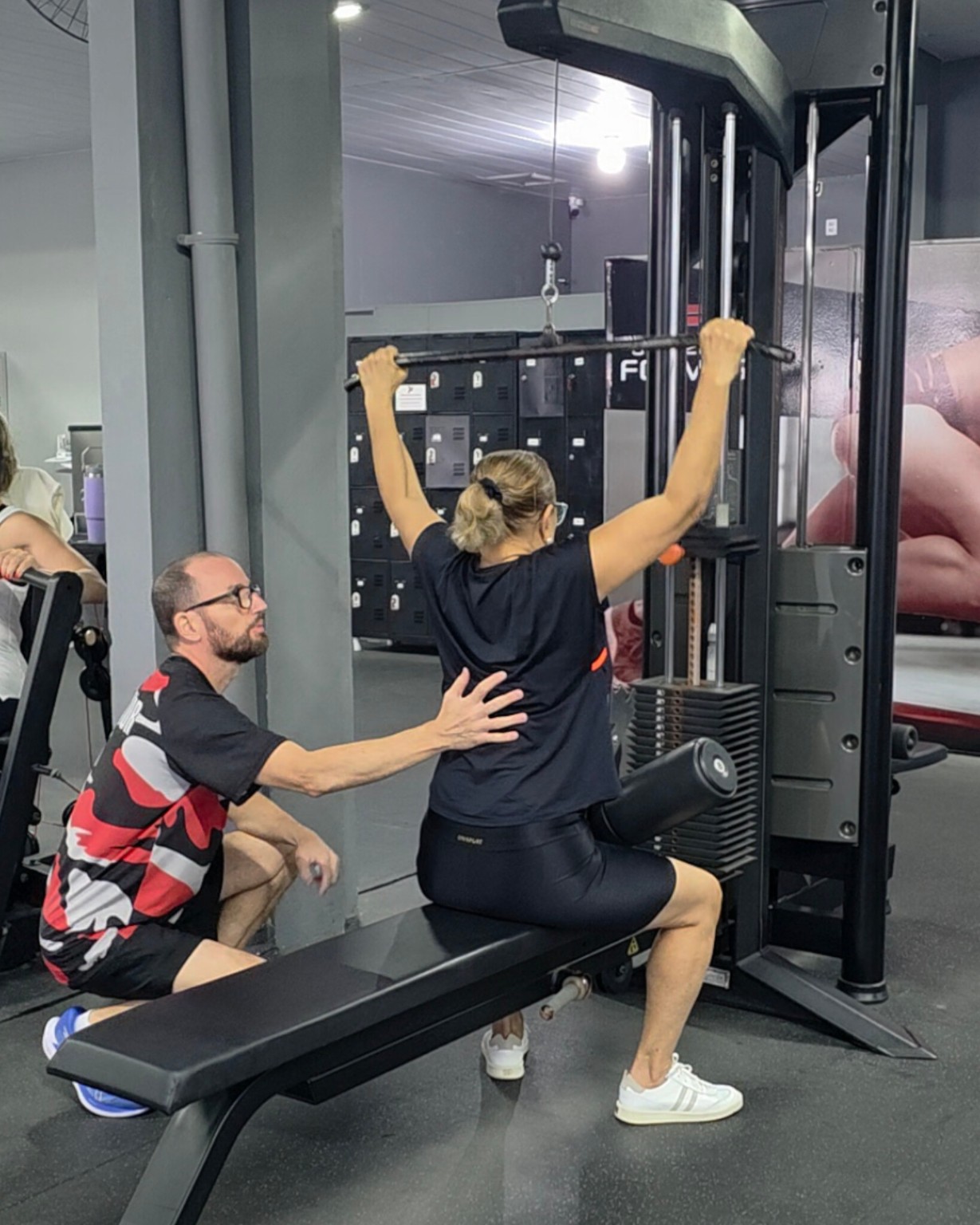 Professor acompanhando uma aluna durante o treino de musculação